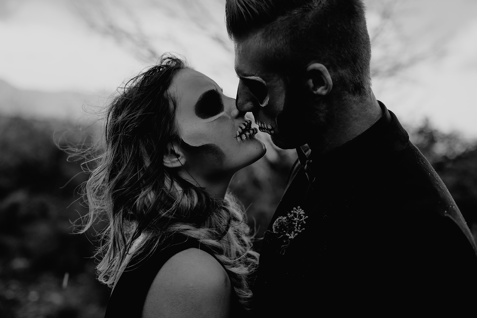 a couple nearly kissing dressed in all black with skull face makeup for a wedding