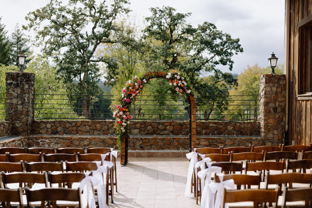 Maysara Winery Wedding ceremony setup. A wedding arch covered in colorful flowers on the upper patio